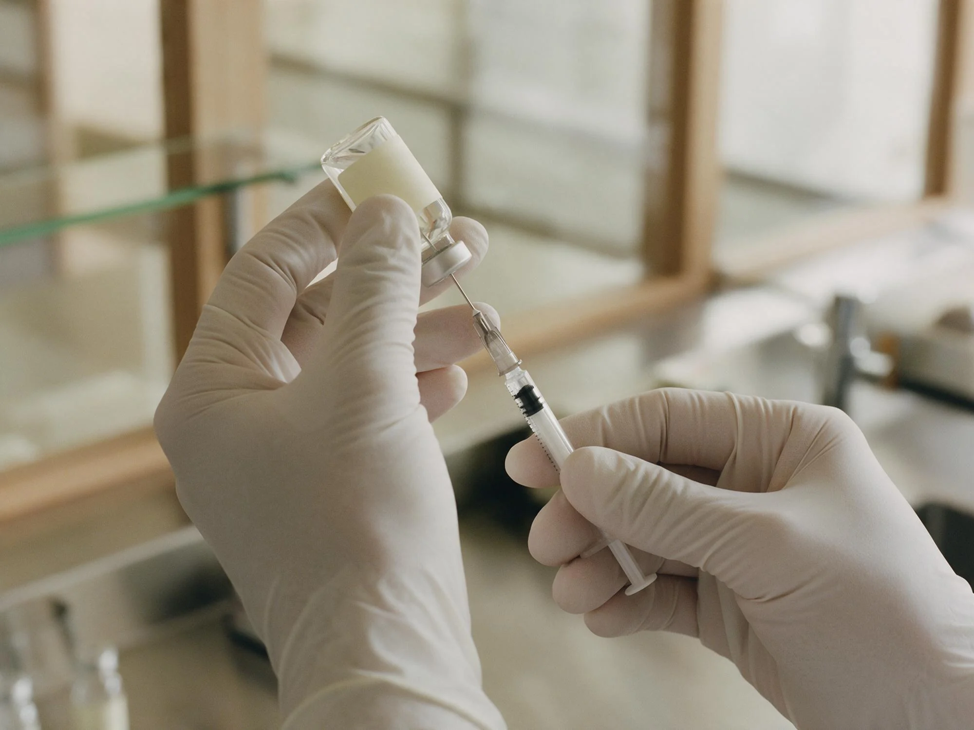 Gloved hands filling a glass vial at the compounding bench